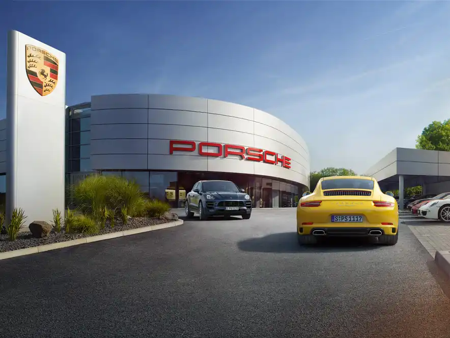 Un centre Porsche à l'arrière-plan et plusieurs voitures Porsche dans les environs.